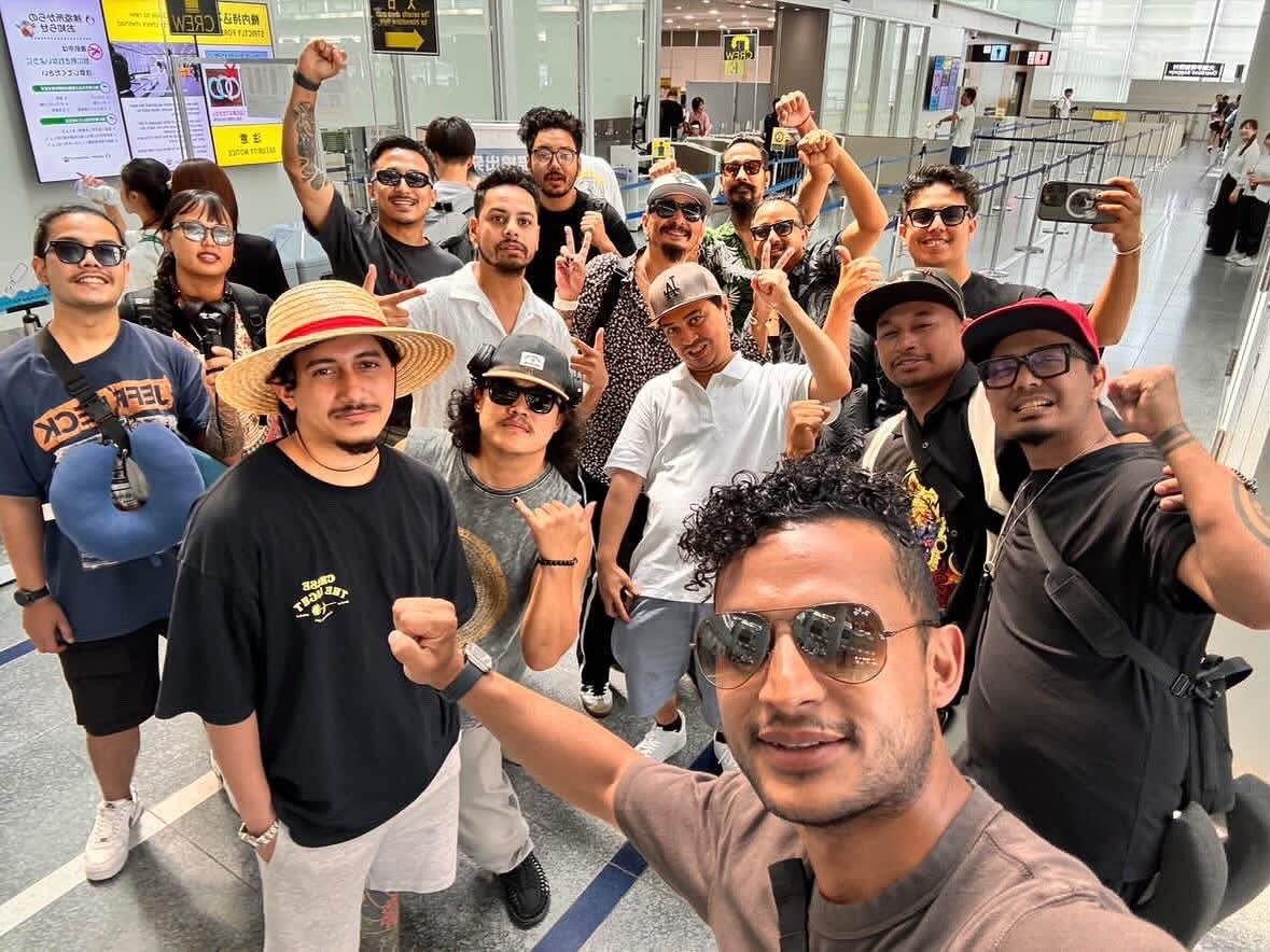 A large group selfie of the band Cobweb and their crew in an airport departure hall, fists raised