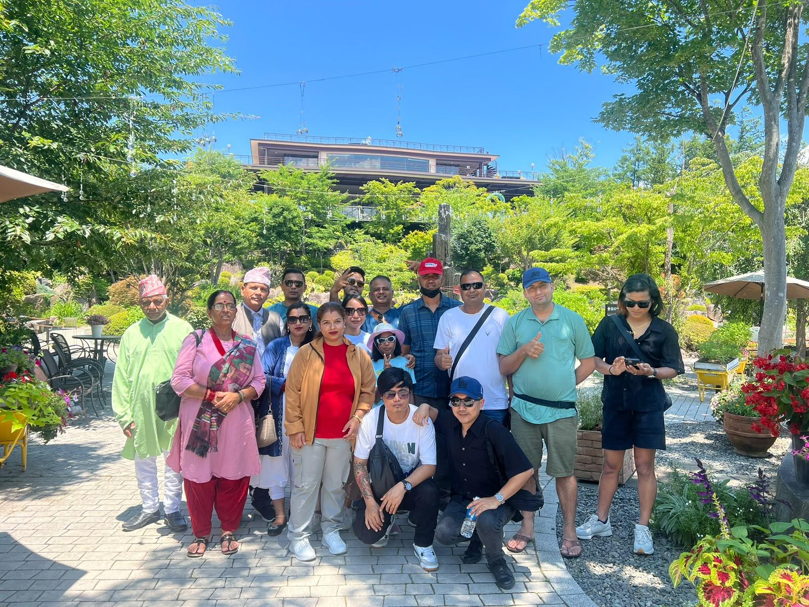 A group including elders in traditional Nepali dress in a sunlit Japanese garden