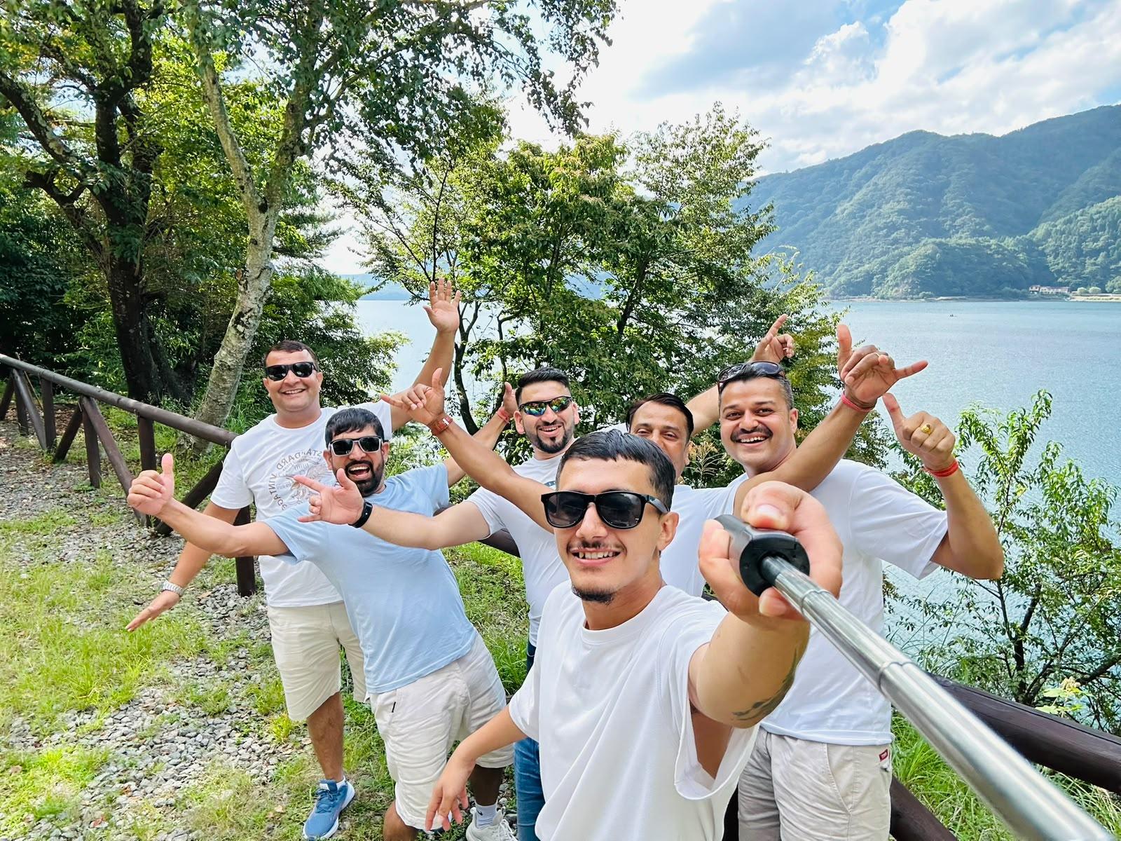 Six travellers in white shirts with their arms raised beside a lake