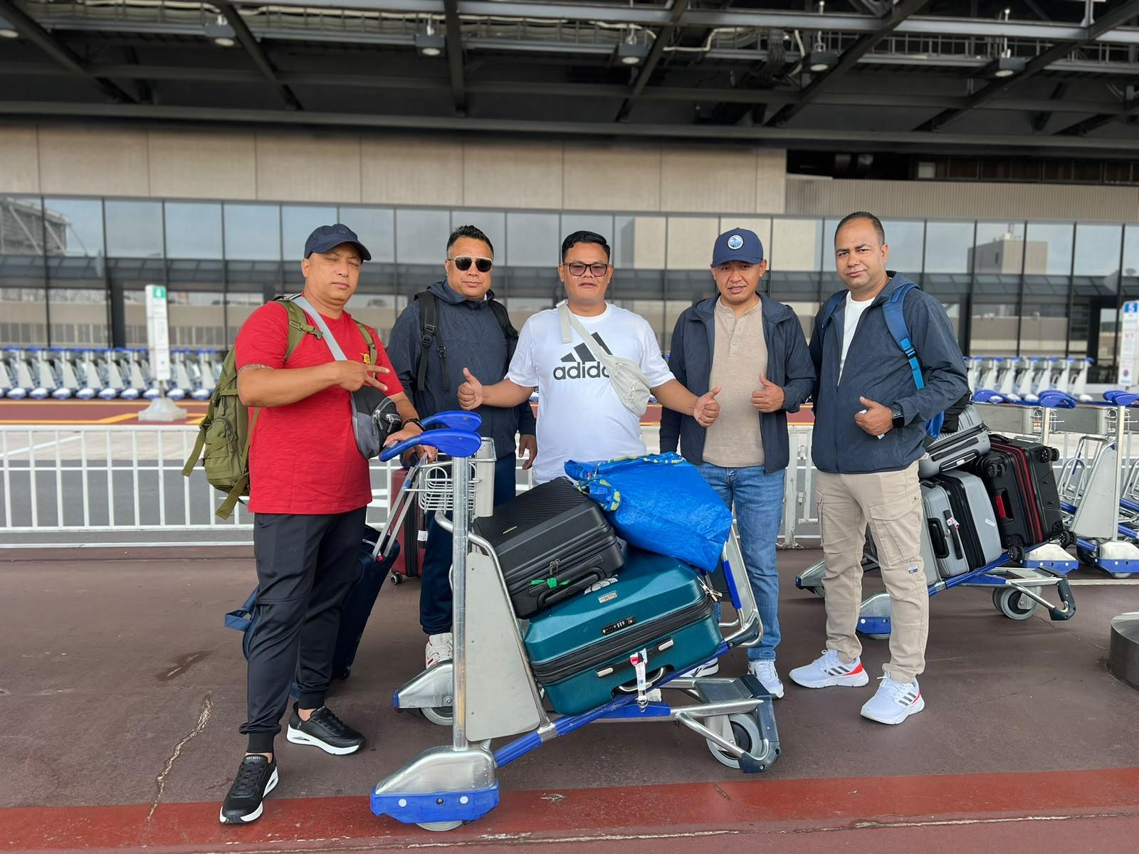 Five travellers with luggage trolleys outside the airport terminal